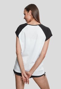 Camiseta de algodón blanca y negra con mangas raglán cortas, textura suave y escote redondeado, vista desde la parte posterior.