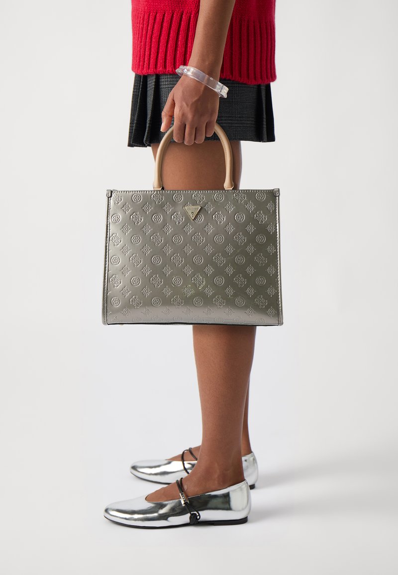 Borsa grigia in rilievo con manici beige, caratterizzata da un motivo geometrico. Abbinata a scarpe metalliche argento e una gonna nera texture.