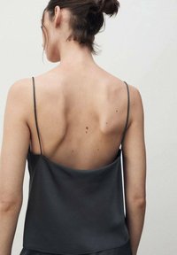 Camisole en satin noir avec de fines bretelles, présentant une coupe ample et une texture lisse. Le design au dos dévoile les épaules et le haut du dos.