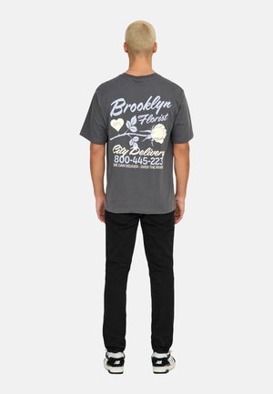 Gray cotton t-shirt with a graphic design featuring flowers and text, paired with black pants and black shoes. Back view only.