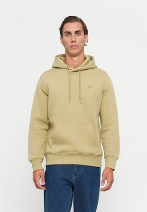 Kapuzensweatshirt in gedämpftem Olivgrün, aus weichem Material gefertigt, mit einer Fronttasche und gerippten Bündchen, sowie einem kleinen Logo auf der Brust.