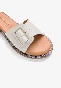 Weiße Leder-Sandale mit einem breiten Riemen, der mit einer großen rechteckigen Schnalle versehen ist. Genoppte beige Innensohle mit einem gemusterten Randverlauf.