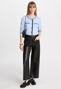 Cardigan lavorato a maglia di colore blu chiaro con dettagli e bottoni neri, abbinato a pantaloni in pelle nera a vita alta con gamba larga e scarpe nere lucide.