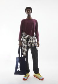 Bordeaux langemouwen shirt, blauw en beige geruit hemd om de taille geknoopt, zwarte broek, gele en blauwe sneakers, marineblauwe tas met wit logo.