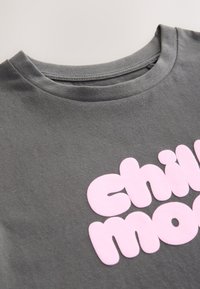 Maglietta grigia in cotone con una grande scritta grafica rosa tenue che recita "chill mode" sul davanti, con un font giocoso.