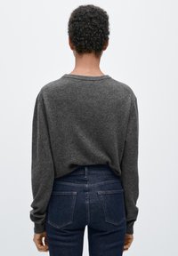 Dunkelgrauer Pullover aus weichem Strick mit lockerem Schnitt und langen Ärmeln. Kombiniert mit dunkelblauen Jeans mit Gesäßtaschen und figurbetonter Silhouette.