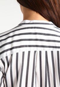 Camicia a righe con una base bianca e righe verticali grigie scure, in un tessuto morbido e con colletto classico sul retro.