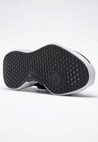 Svart gummisula med hexagonalt mönster, texturerad för grepp, med en vit mellansula och rundade kanter. Reebok-logotyp på sidan.