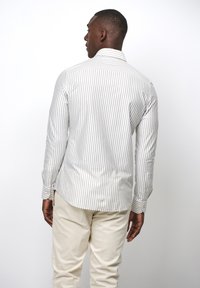 Camisa de manga larga a rayas en blanco y gris claro con cuello abotonado; cuenta con un dobladillo redondeado y puños abotonados; textura de tela suave.