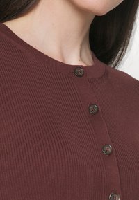 Bordeaux geribbelde cardigan met een ronde halslijn en vijf donkere knopen, met een gestructureerde stof en een nauwsluitend ontwerp.