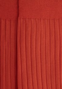 Tessuto a coste rosso che mostra una texture morbida con righe verticali e una parte superiore liscia. Il materiale sembra elastico e leggero.