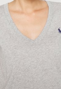  camiseta gris de cuello en V hecha de algodón suave con un acabado texturizado y un pequeño logo en azul marino en el área del pecho izquierdo.
