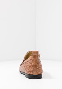 Brown leather loafer with a textured crocodile pattern, flat sole, and minimal stitching details, featuring a low-cut back for easy wear.