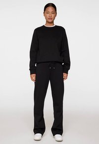 Sweatshirt noir à encolure ronde et manches longues, assorti d'un pantalon de jogging noir avec un cordon de serrage ajustable.