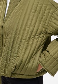 Olivově zelená prošívaná bomber bunda s vertikálním prošíváním, s předním zipem a volně střiženými rukávy. Texturovaný, lehký materiál.