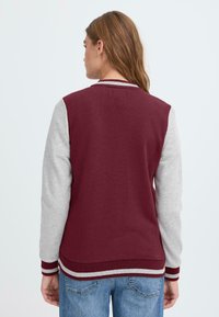 Maroon och grå varsityjacka med grå ärmar, ribbade manschetter och randig krage. Material av bomullsblandning; avslappnad passform och design.