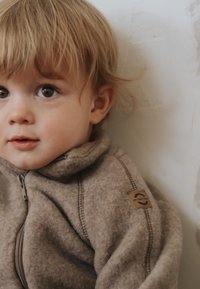 Brun fleecejakke med lynlås og høj krave. Bemærkelsesværdig tekstur og syningsdetaljer. Har et tanfarvet logopatch på ærmet.