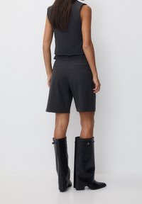 Czarnoszary, dopasowany zestaw kamizelki i szortów, z wysokimi do kolan, czarnymi skórzanymi botkami o gładkiej fakturze i minimalnymi akcentami metalowymi.