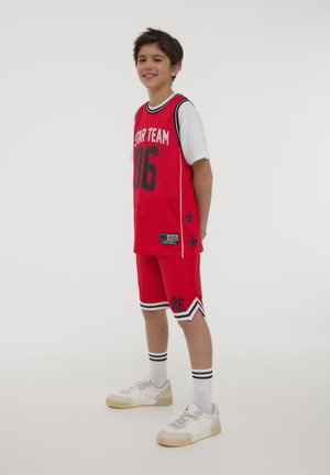 Maglia da basket rossa con dettagli neri, con la scritta "STAR TEAM" e il numero "86", abbinata a pantaloni corti coordinati e scarpe da ginnastica bianche.