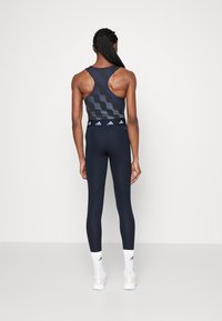 Leggings atletici blu abbinati a una canotta con motivo a onde scure. Entrambi gli articoli presentano una silhouette aderente e uno stile sportivo.