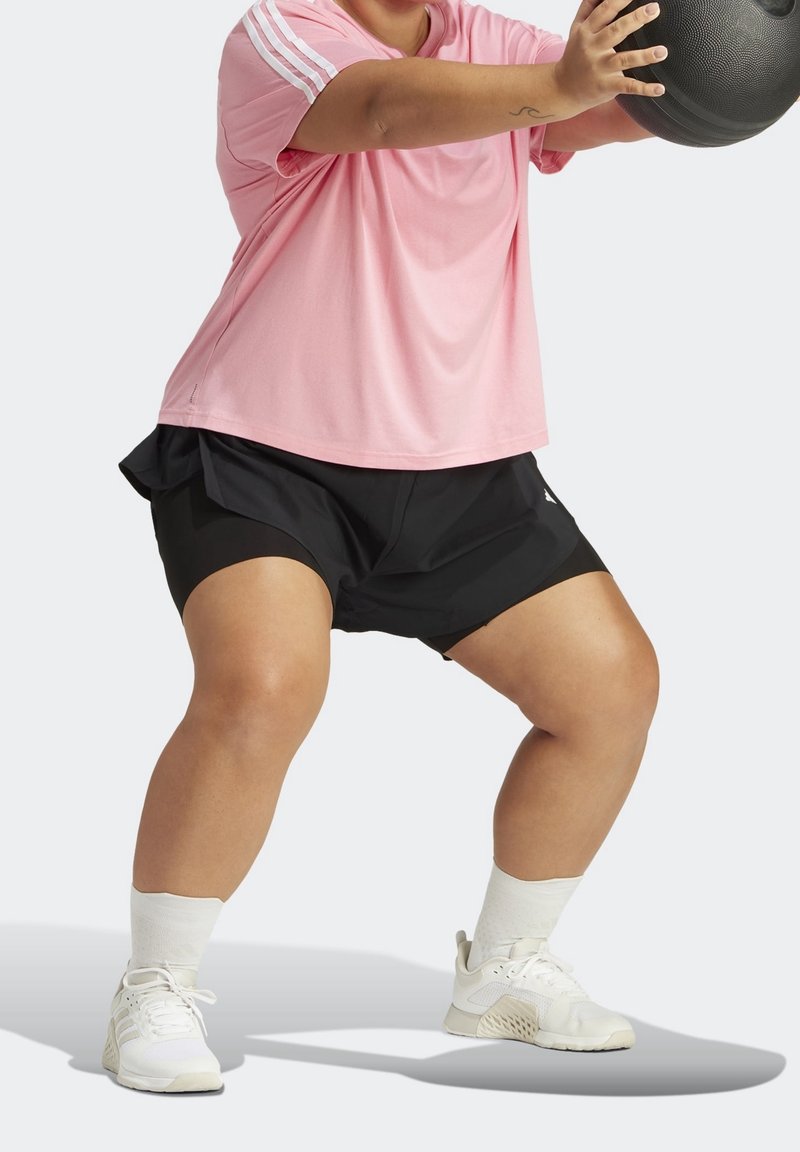 Camiseta deportiva rosa con rayas blancas, pantalones cortos negros con diseño en capas y zapatillas deportivas blancas con acentos texturizados.