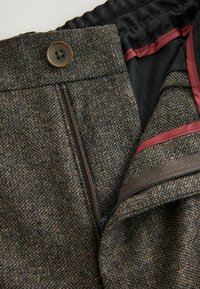 Tweed jacket featuring a brown and black herringbone pattern, bronze button, and burgundy lining with a zippered pocket.