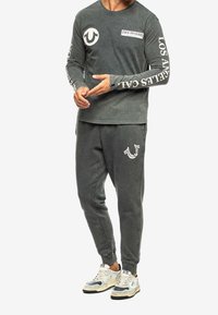 Grijze lange mouwen shirt met logo detail, gecombineerd met bijpassende grijze jogpants. Heeft ribgebreide manchetten en een relaxed fit, met sneakers.