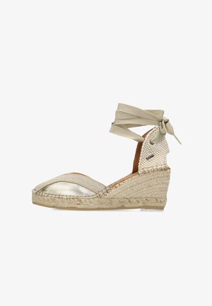 Beige espadrille wedge schoen met een metallic teenkap, geweven hak en een zachte stoffen enkelband. Beschikt over een jute gewikkelde zool.