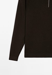Pull noir à manches longues avec une partie visible d'une fermeture éclair argentée en haut, tissu en maille uni, ourlet et poignets côtelés.
