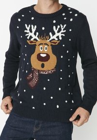 Mörkblå tröja med renmotiv som har ett brunt ansikte, horn och en mönstrad scarf, accentuerad med vita snöflingemönster.