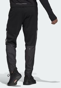 Svarta idrottsbyxor med en lätt avsmalnande passform, med blanka svarta sidopaneller, reflexdetaljer och zippered nederdelar. Strukturerad tyg.
