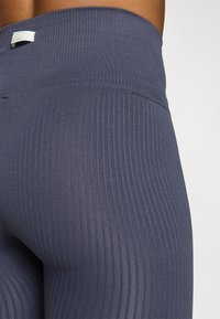 Leggings a coste di colore blu navy con vita alta, caratterizzati da una texture liscia e un piccolo etichetta sul retro.