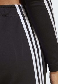 Čierne joggers z jemnej látky s tromi bielymi vertikálnymi pruhmi po stranách, so snug pásom a jemnou textúrou.