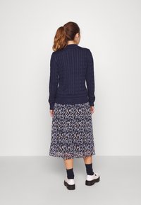 Navy cable-knit sweater with ribbed cuffs and hem paired with a floral, knee-length skirt featuring blue, black, and white patterns. White shoes.
