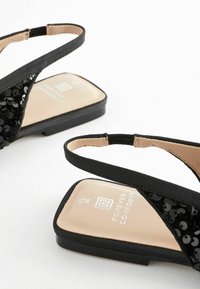 Sandales plates noires avec un dessus pailleté, de fines sangles noires et une semelle intérieure rembourrée couleur beige. Conçues pour le confort avec une forme élégante et minimaliste.