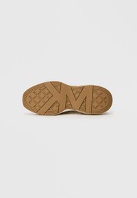 Talpa de sneaker bej cu un profil texturat și un model mare cu logo-ul "MK", prezentată pe un fundal alb simplu.