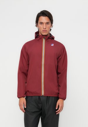Veste coupe-vent bordeaux avec capuche, fermeture éclair ornée de rayures jaunes et blanches, et poignets élastiqués. Matériau léger avec détail de logo.