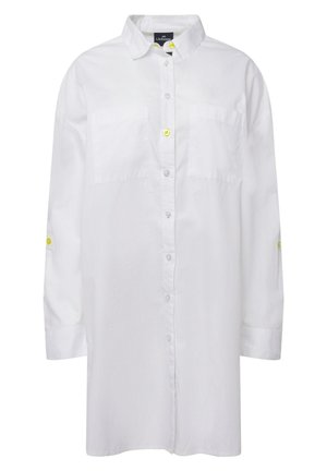 Camicia bianca con colletto, due tasche frontali e bottoni gialli a contrasto. Presenta maniche lunghe e una vestibilità ampia.
