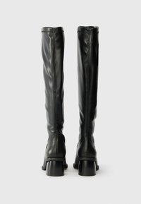 Térdig érő fekete bőr csizmák sima felülettel, diszkrét varrási részletekkel és masszív sarkakkal. Sima, testhezálló dizájn a modern megjelenés érdekében.
