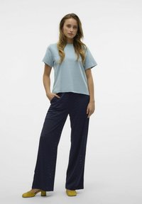 Vaaleansininen lyhythihainen t-paita yhdistettynä tummansinisiin viivakuosisisiin leveälahkeisiin housuihin ja keltaisiin kenkiin. Asusteessa on rento istuvuus ja taskut.