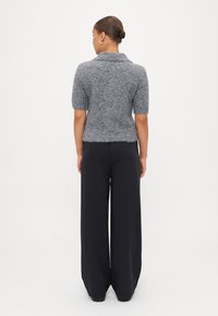 Short-sleeve, gray knitted sweater with a collared neck and fuzzy texture, paired with high-waisted, wide-leg black trousers.
