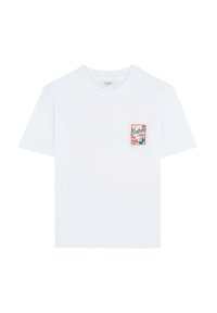 T-shirt en coton blanc à manches courtes, avec une pièce brodée colorée sur la poitrine gauche présentant des éléments de design tropical.
