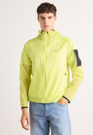 Lightweight, bright yellow jacket with a fitted hood, zippered front, and a side pocket. Made of smooth, breathable fabric.