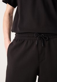 Top sportivo nero con vestibilità rilassata, abbinato a pantaloni della tuta neri con coulisse, dotati di cintura elasticizzata e tasche laterali.