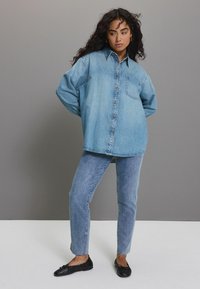 Lichtblauwe denim oversized overhemden met knopen en een borstzak, gecombineerd met bijpassende skinny jeans en zwarte platte schoenen.