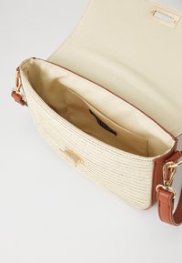 Kabelka na rameno z hnědé umělé kůže se tkaným krémovým texturovaným povrchem, zlatými kovovými doplňky a otevřeným béžovým textilním interiérem.