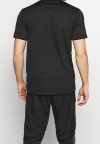 Svart kortärmad t-shirt gjord av mjukt tyg, med rund halsringning och en slät textur, visad på en person från baksidan.