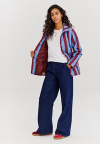 Prošívaná bunda v maroon a modrých pruzích, s kontrastní podšívkou. Kombinována s tmavě modrými širokými kalhotami a červenými botami.