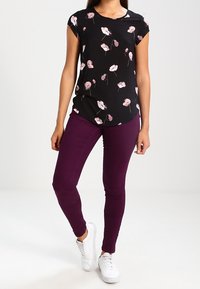 Černá květinová blůza s krátkým rukávem a vzory růžových a bílých květin, zkombinovaná s fitted fialovými džíny a bílými teniskami.