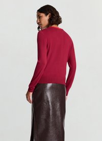 Red long-sleeve sweater with a fitted design and ribbed cuffs, paired with a shiny, dark brown leather skirt featuring a side slit.